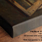 The image is a close-up of a wooden frame with a painting on it, placed on a wooden surface.